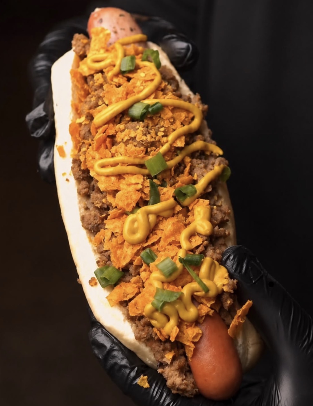 Loaded hot dog topped with ground beef, chips and mustard
